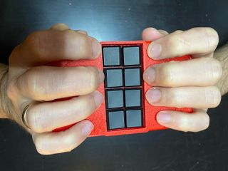 Hände auf der Oskar Fein Braille-Tastatur mit Händen neben den 8 Tasten. Die Tasten sind schwarz, das Gehäuse ist rot der Hintergrund ist schwarz.
